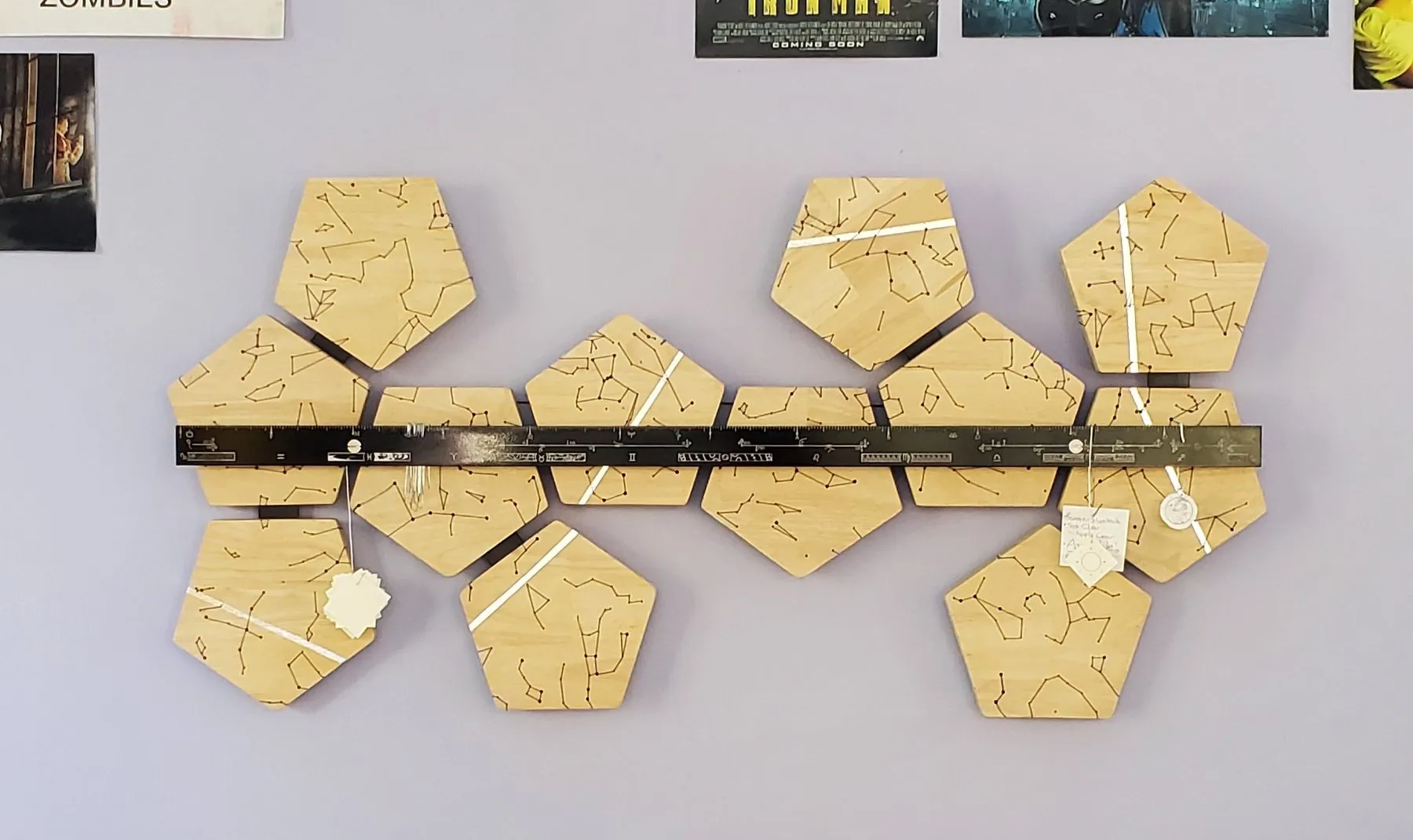 The finished 'Verse hanging on a wall. Twelve wooden pentagons engraved with constellations, linked by a black band.